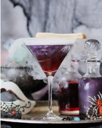 Purple cocktail in martini glass with dry ice and fake spider decorations.