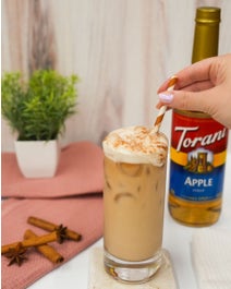 Iced apple pie chai with foam on a table being stirred with a straw.