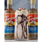 Banana split milkshake in a glass topped with bananas, nuts, chocolate sauce.