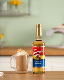 Banana coffee in a mug topped with whipped cream and cookie.