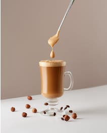 Coffee in a mug with hazelnuts and foam scooped on top.