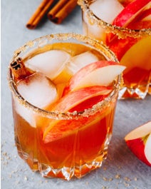 Apple cocktail with sugar rim and cinnamon sticks.