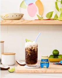 Coconut Dirty Soda in a glass with ingredients on a table.