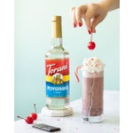 Dark chocolate peppermint maraschino shake with whipped cream topped with a cherry on a table next to syrup bottle.