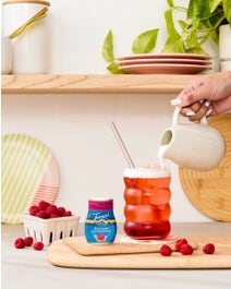Raspberry Dirty Soda on a table with ingredients and cream poured on top.