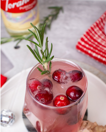 Diamond cranberry smash in a glass with cranberry ice cubes and a rosemary sprig for garnish.